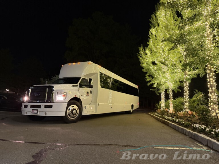 White luxury transformer party bus at night, lit by trees.