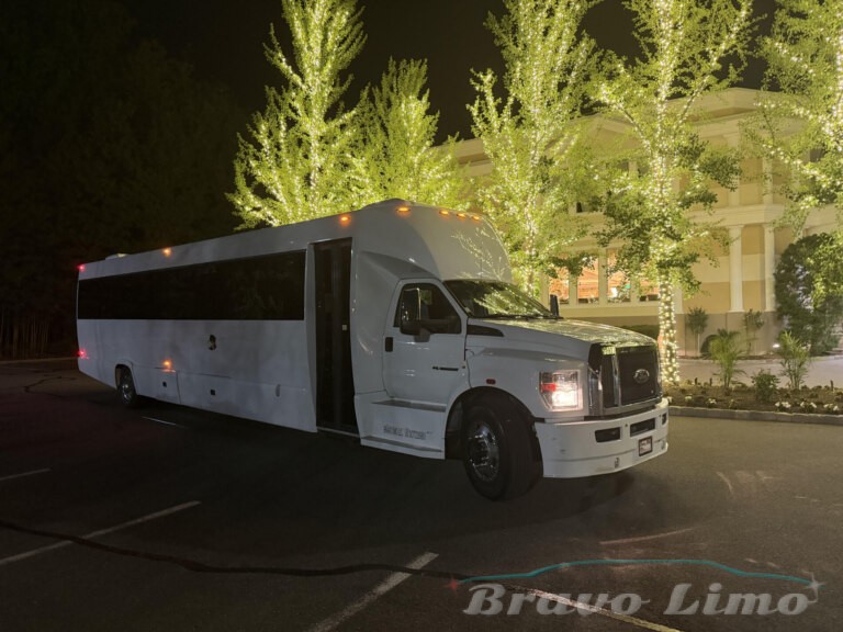 White luxury party bus at night, illuminated by decorative lights.
